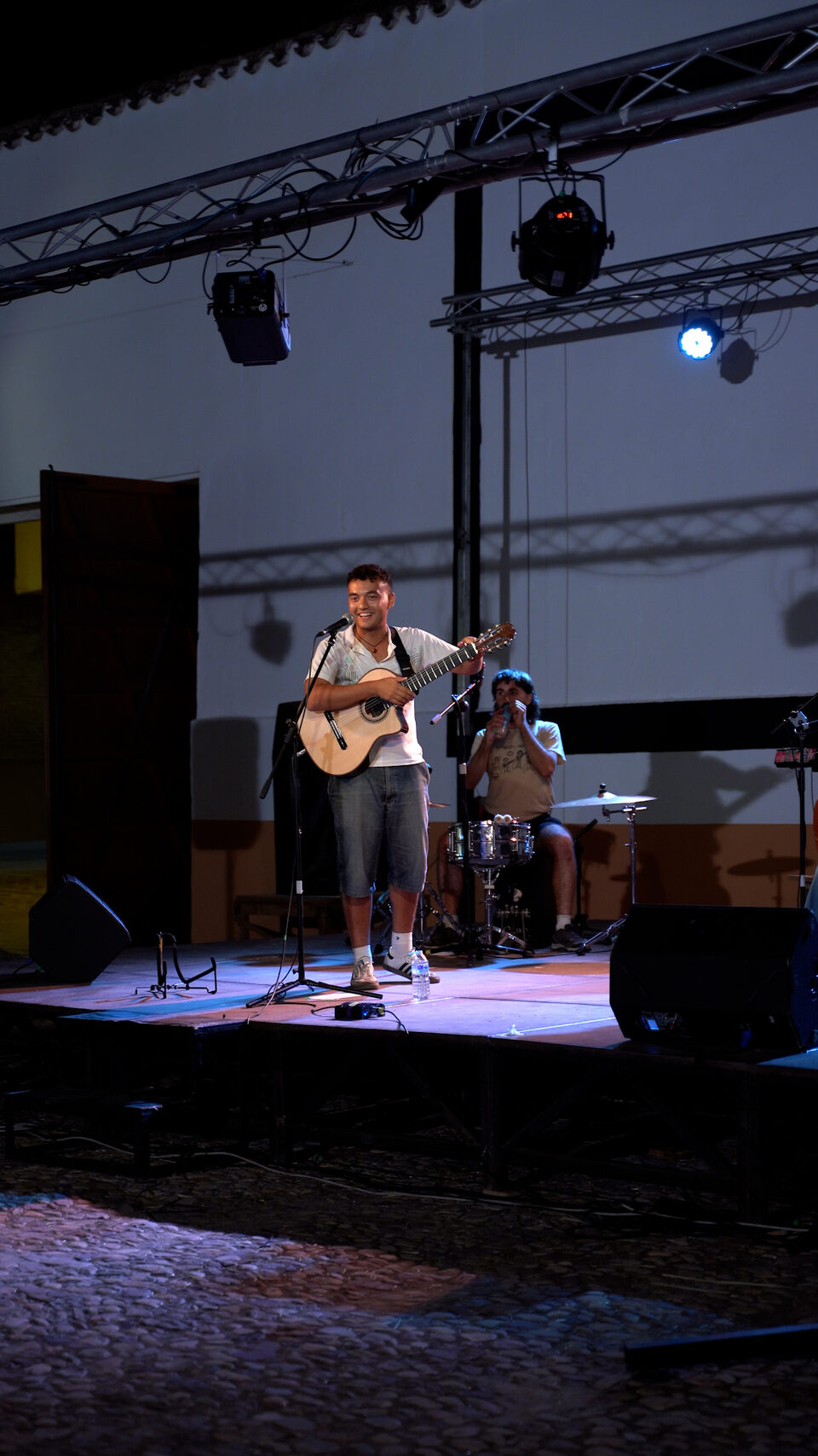 David cantando con la guitarra en un escenario al aire libre, con el percusionista detrás