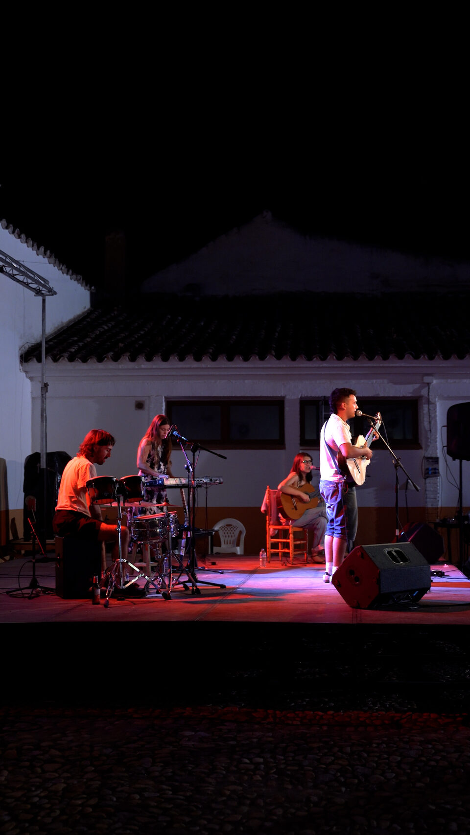 El grupo tocando de noche en un escenario montado delante de una casa encalada