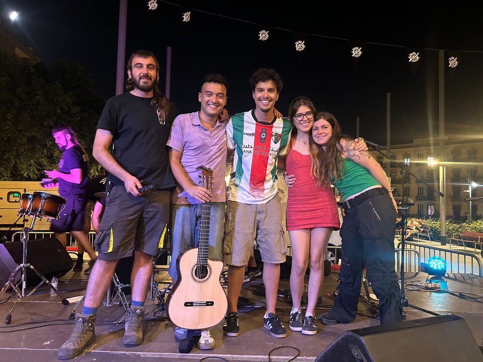 Cinco músicos posando en el escenario al acabar el concierto, con guirnaldas de luces detrás