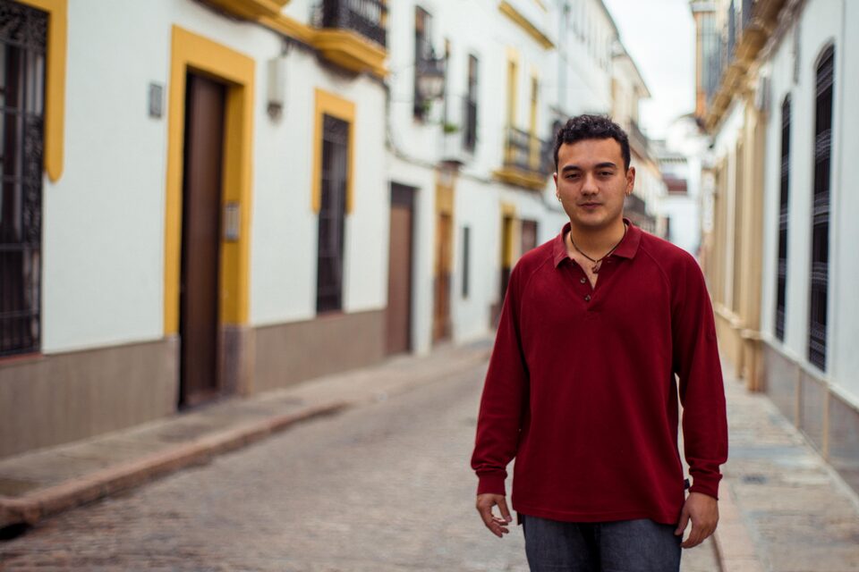 David de pie en una calle empedrada de Córdoba, con las fachadas blancas y amarillas al fondo