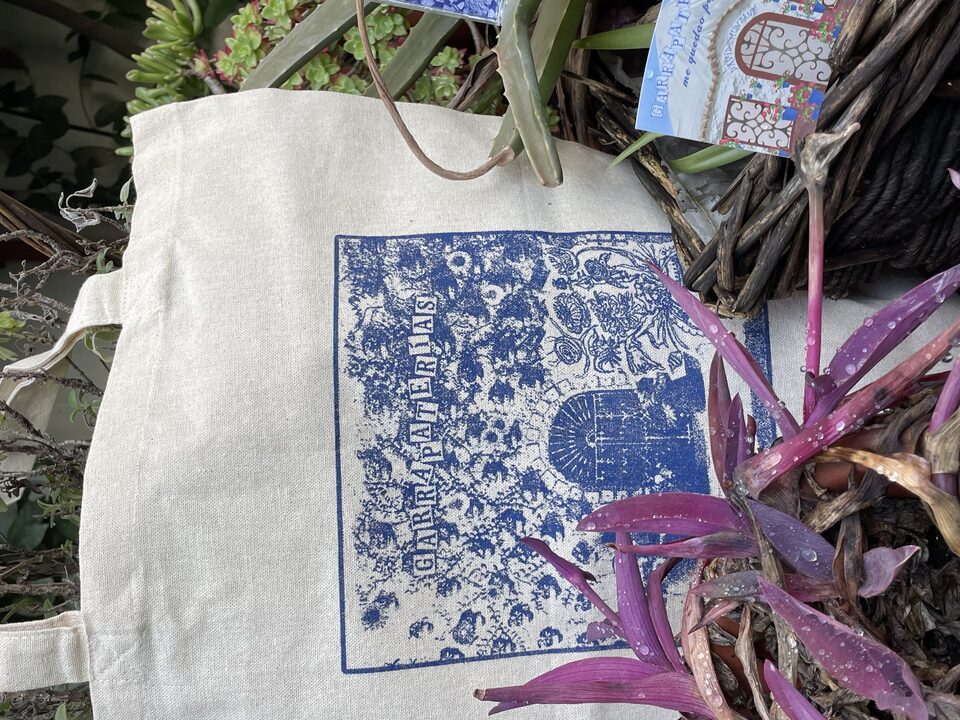 El totebag de lienzo de Garrapaterías, con la portada serigrafiada en azul, entre las plantas del patio